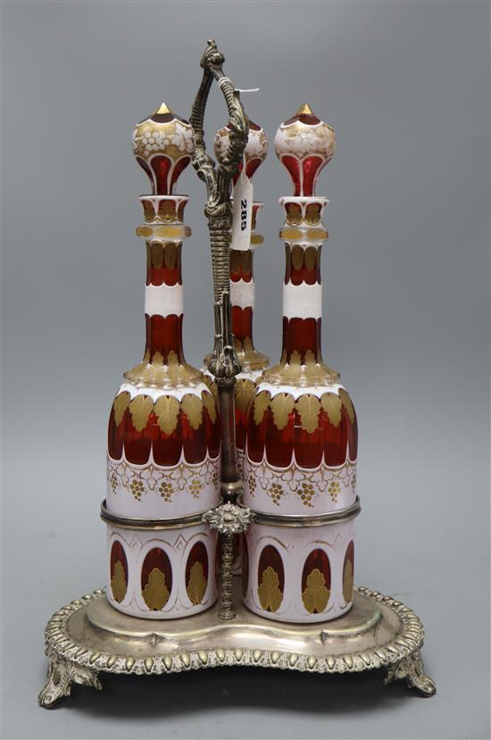 A plated three bottle tantalus, the decanters overlaid glass with gilt decoration, height 37cm